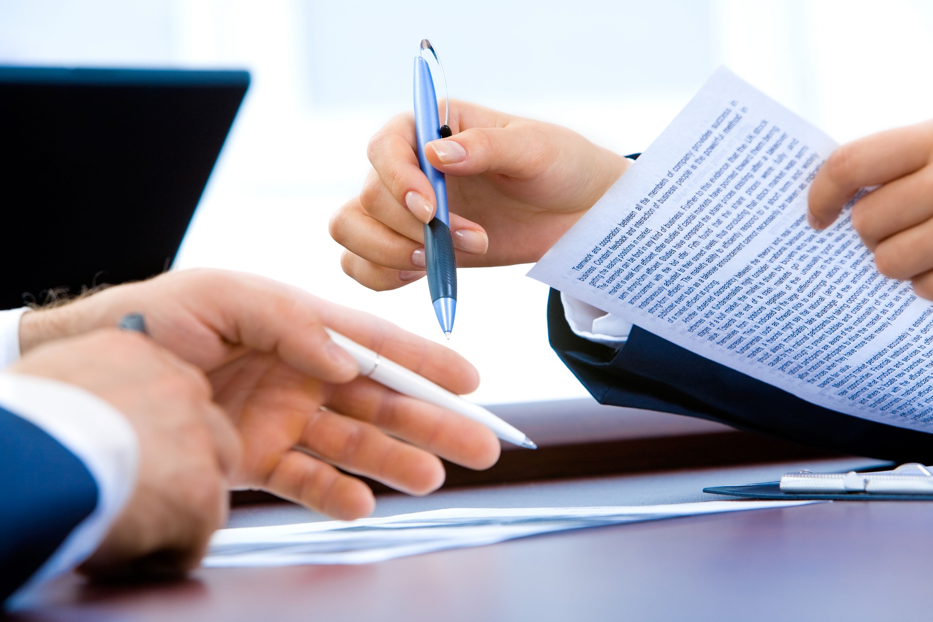 Two professionals at a table reviewing and discussing an insourcing knowledge document; one is pointing at the paper with a pen.