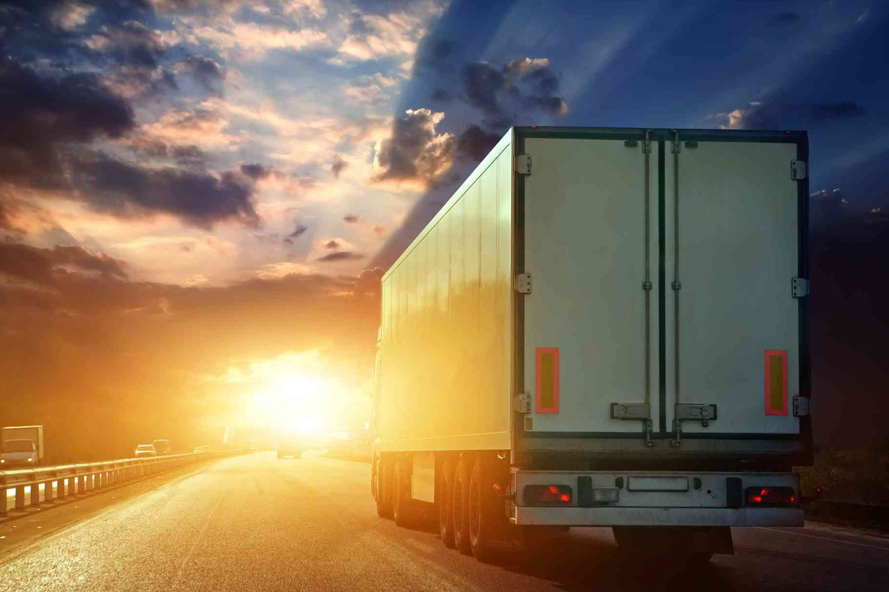 A truck driving on a highway at sunset, with bright sunlight ahead and a clear sky, highlights the functional services of transportation logistics.