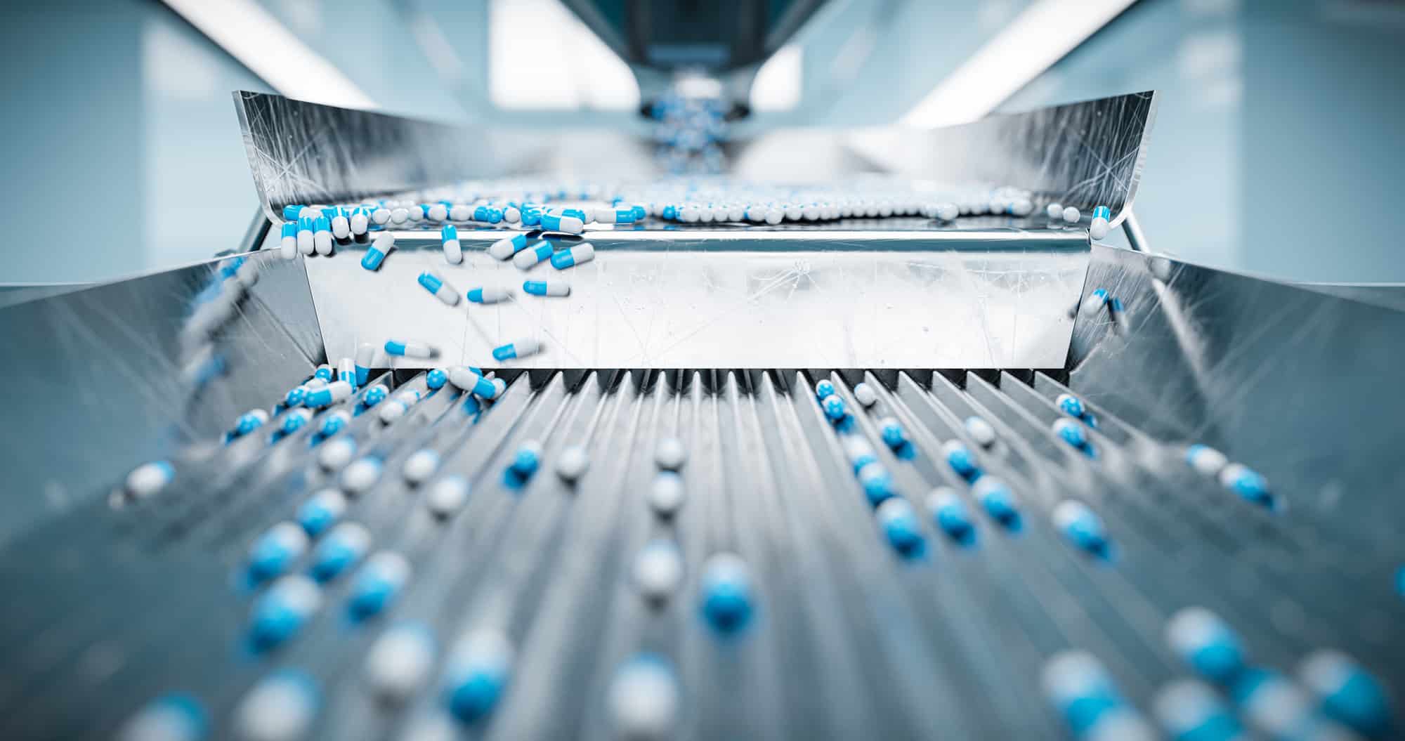 Blue and white capsules in pharmaceutical operations on a conveyor belt in a manufacturing facility.