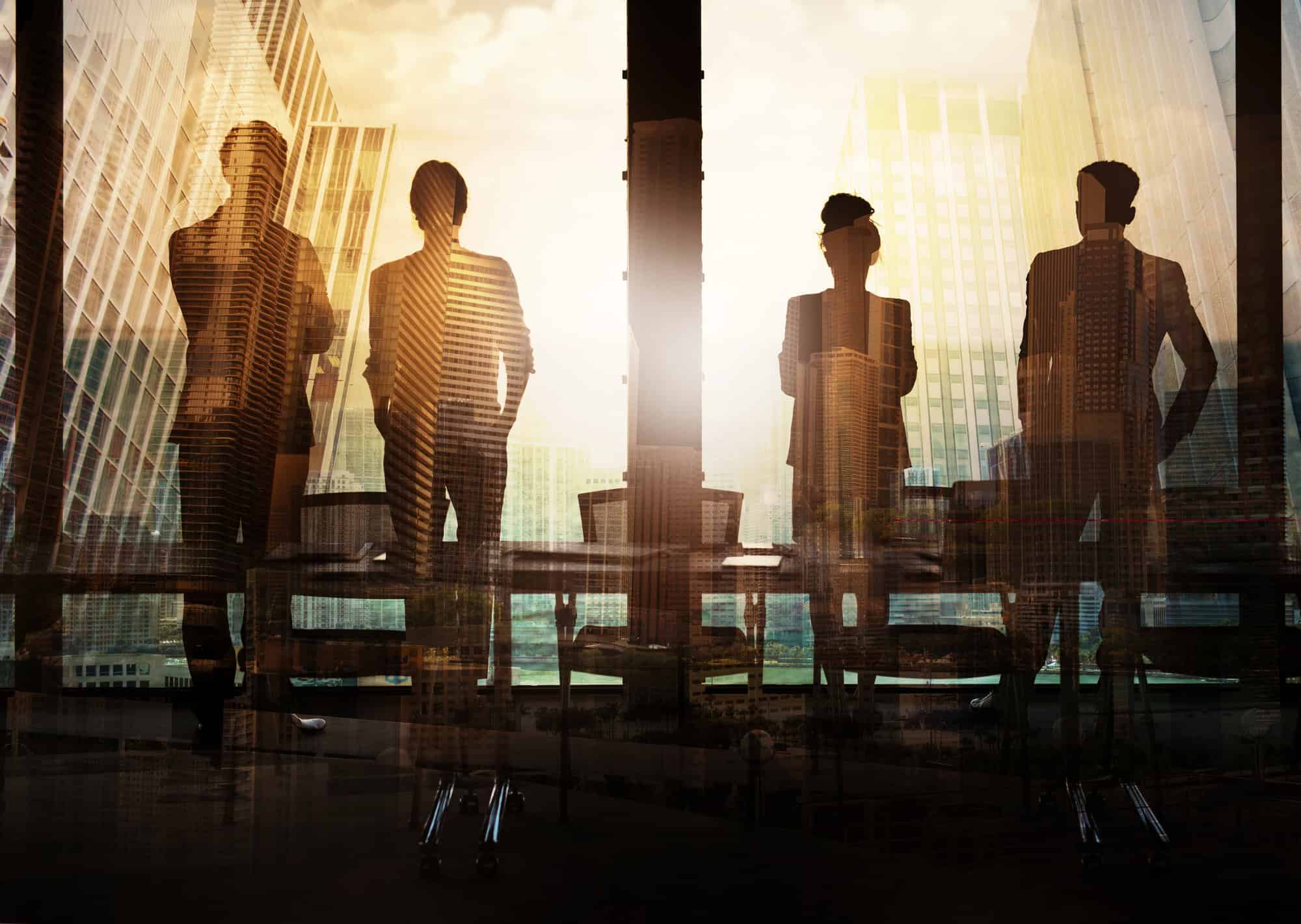 Silhouettes of four people in business attire standing by a window with city buildings in the background.