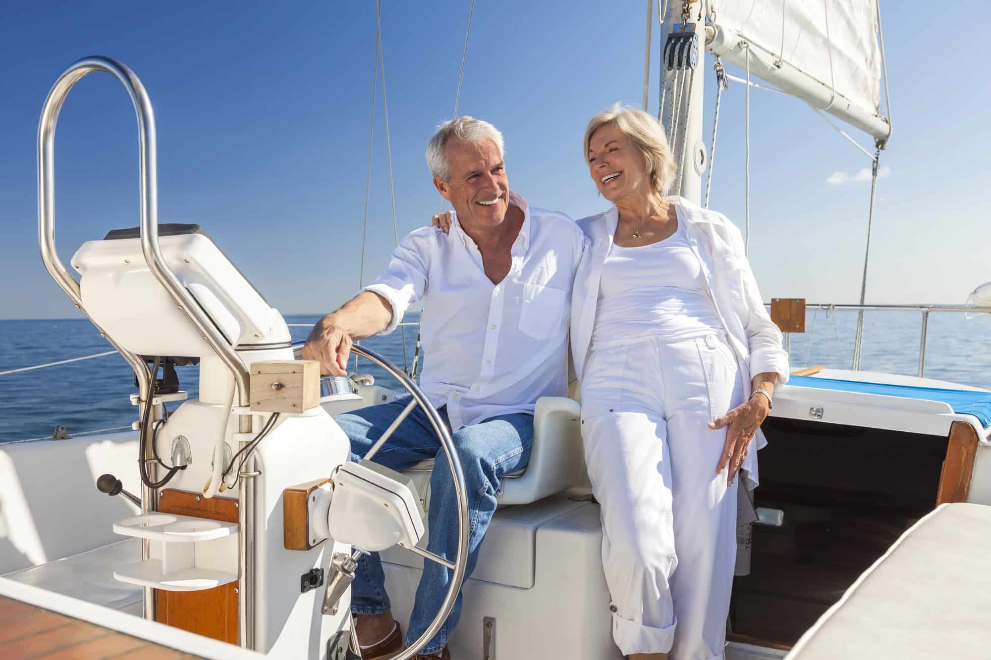An older couple in white clothing sit and smile together on a sailboat under a clear blue sky, reflecting on successful succession planning for their family's future in an uncertain economy.