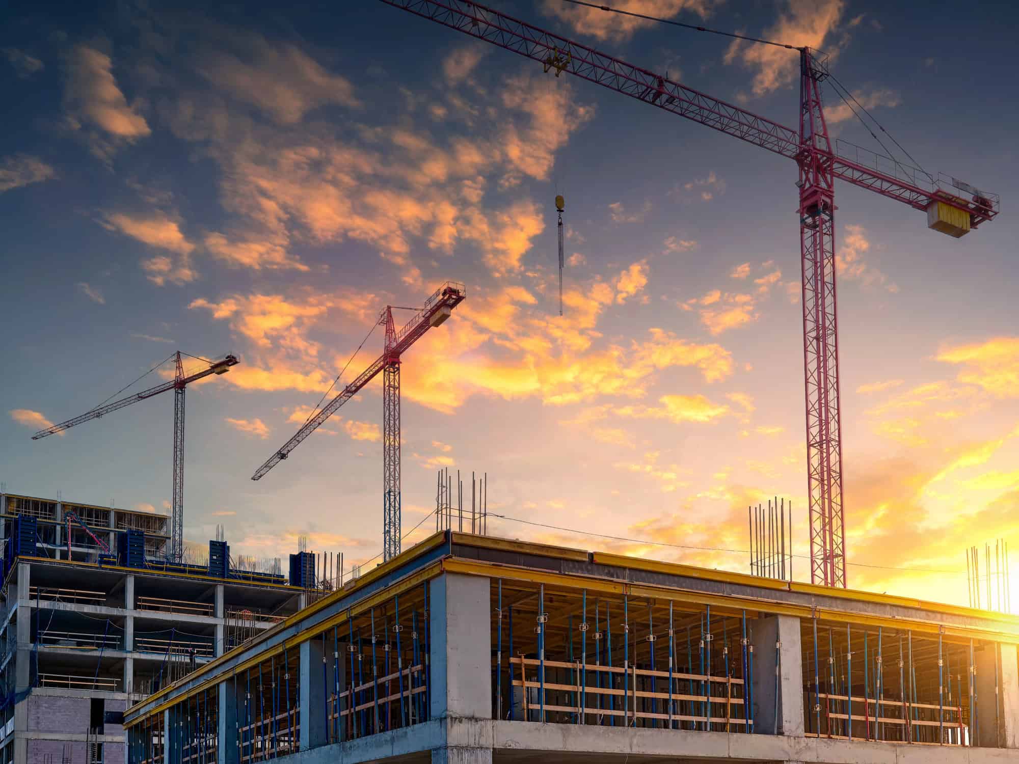 A construction site with cranes and a building frame under a colorful sunset sky, showcasing the growth of construction firms and rising female leadership in 2025.